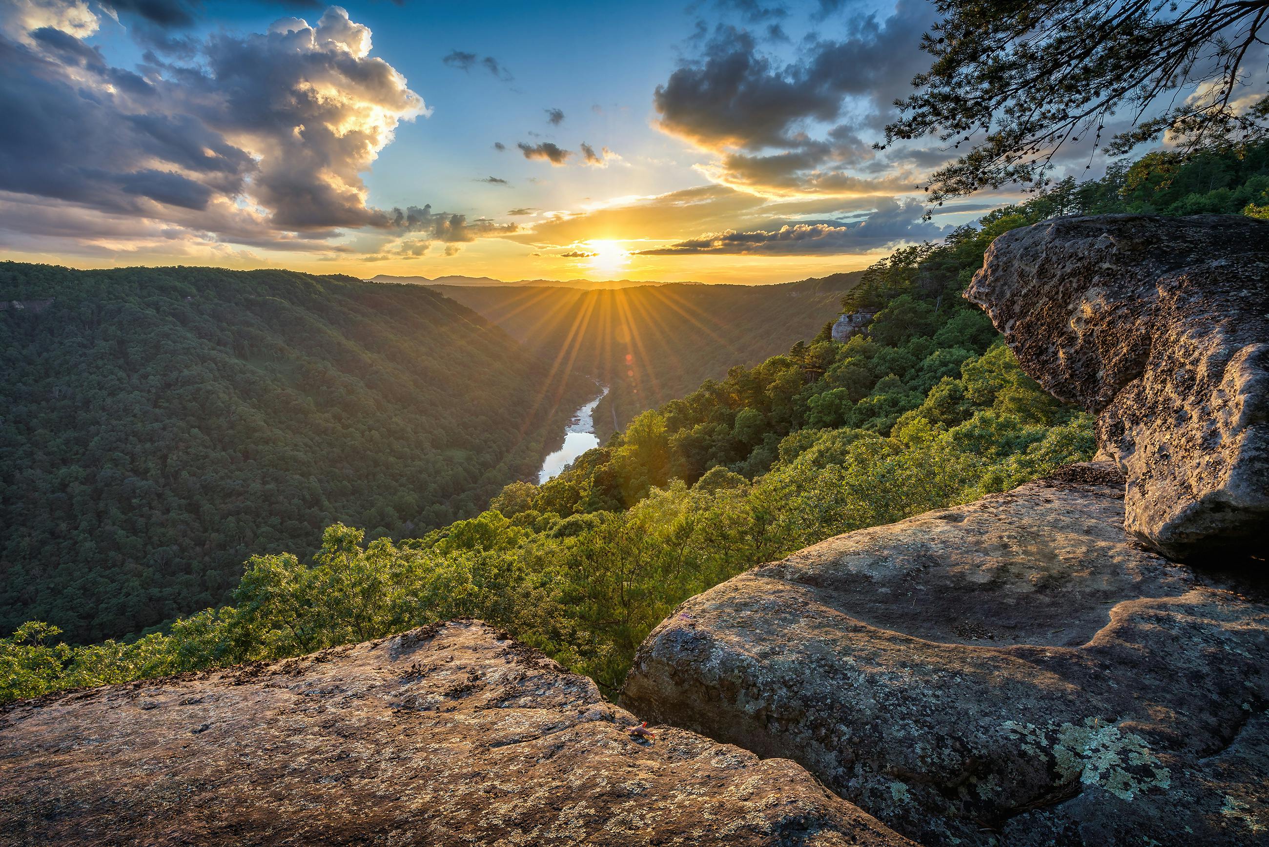 A picture of a sunset on a hill with a river running below through a lush green valley